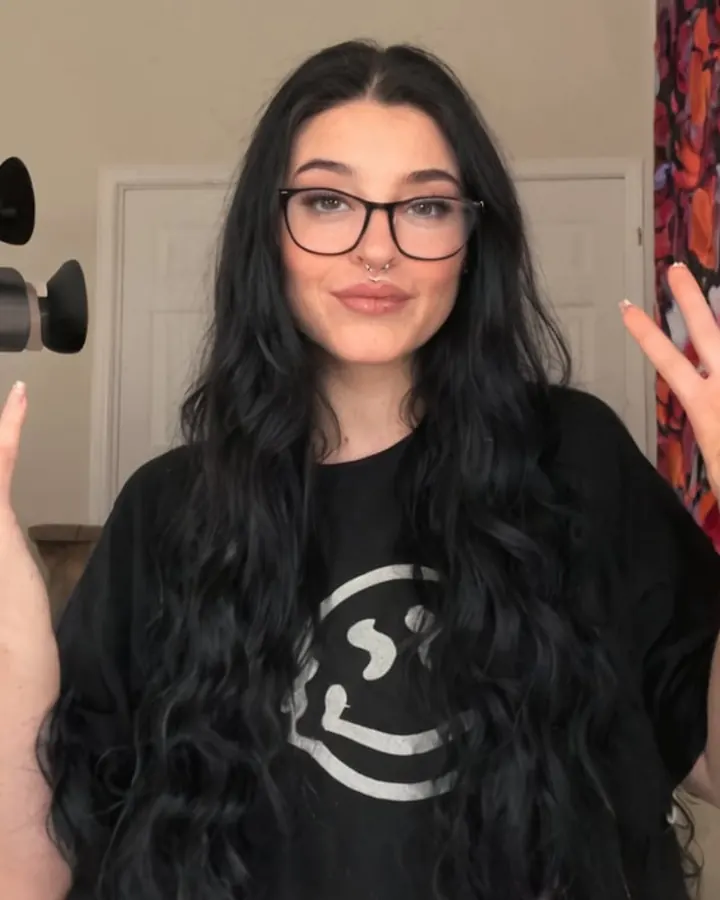 Copine IA aux longs cheveux noirs et à lunettes, en t-shirt noir, sur Dondi AI